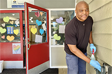 A custodian sanitizes a push plate for an automatic door.