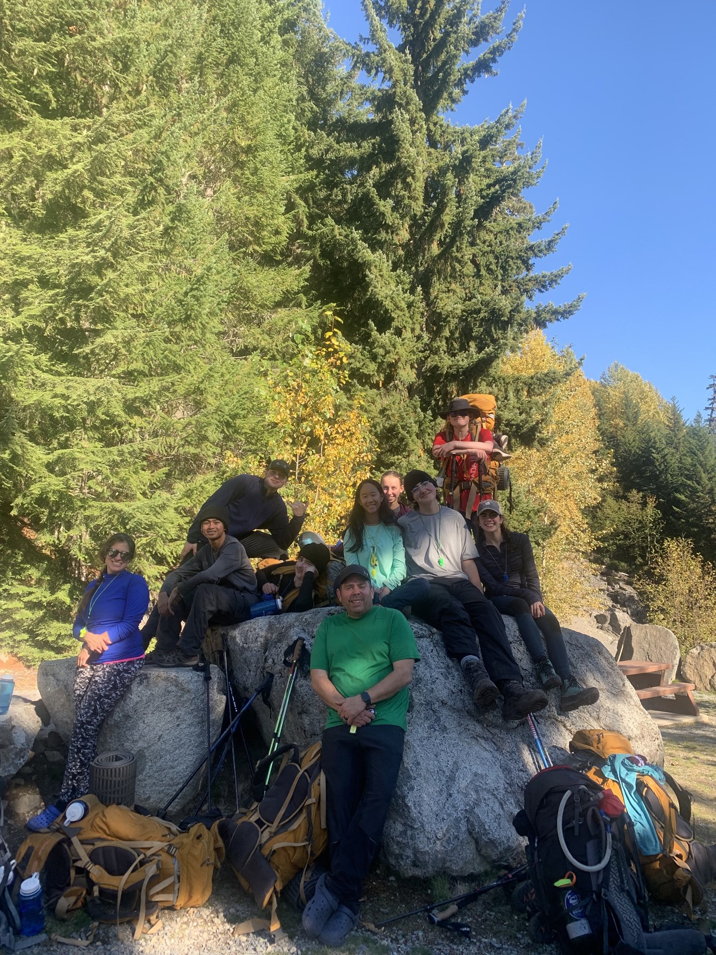 A group of peoepl sit and lean against a large boulder while smiling towards the camera.