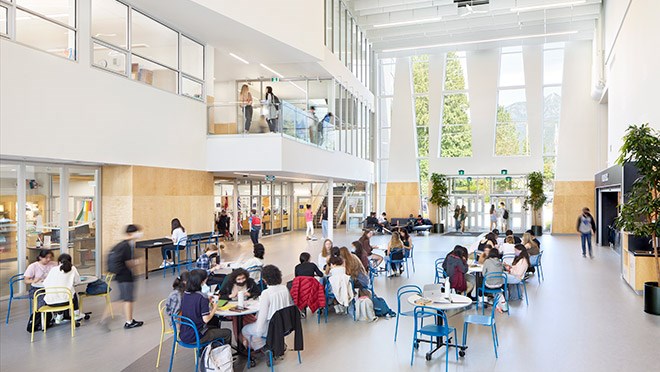 Wide angle photo of an atrium with students sitting at tables.