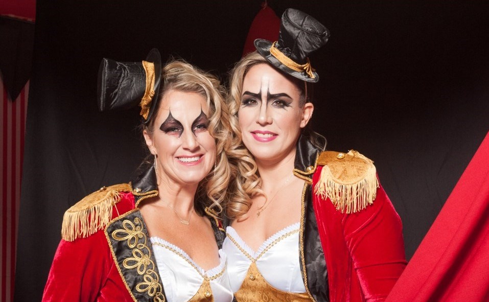 Two women dressed in carnival conductor costumes with striking black eye makeup.