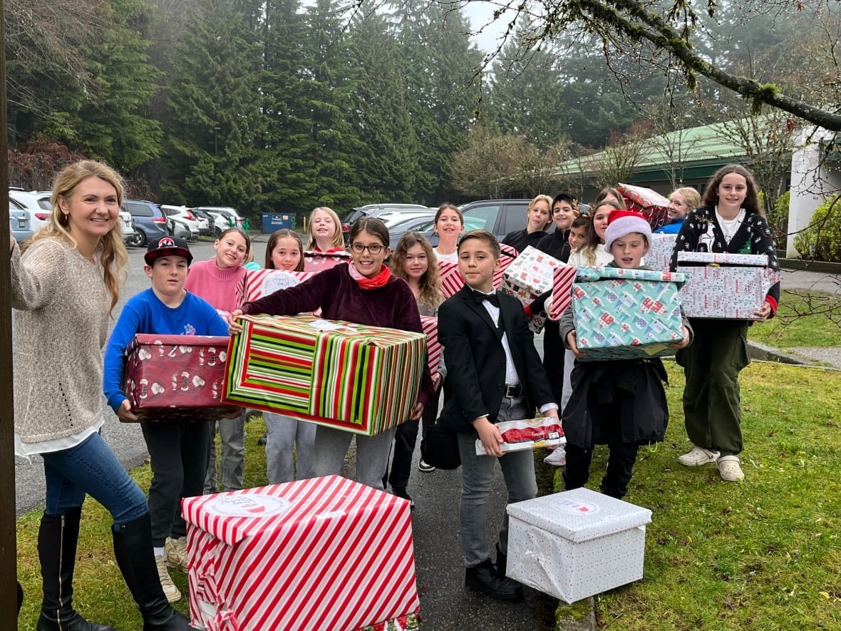 Elementary students stand outside posing with large gift wrapped boxes.