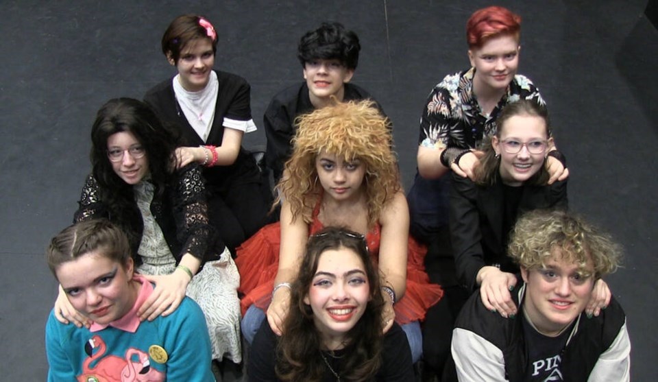 Nine students dressed like they are from the 80's smile towards the camera.