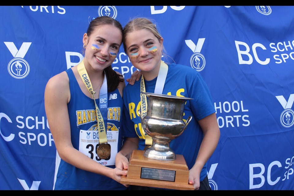 Two girls smile towards the camera holding a large trophy.