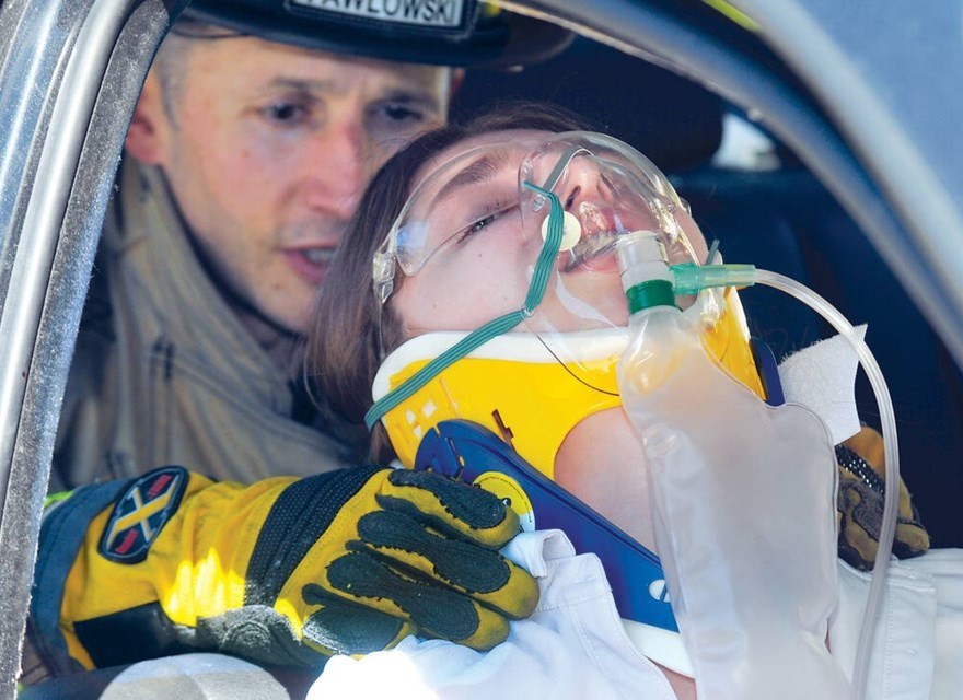 A girl has her head in a neck brace with an oxygen mask being tended to by a fireman.