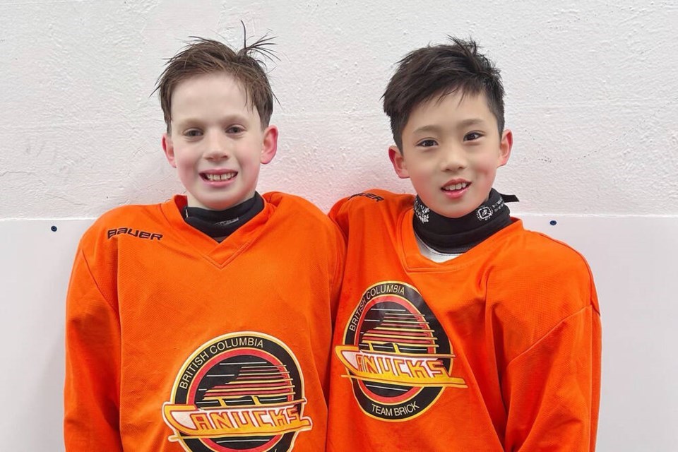 Two elementary aged boys smile towards the camera in orange hockey uniforms.